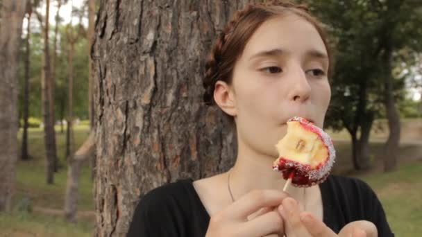 Adolescente chica meditativamente come caramelo manzana . — Vídeos de Stock