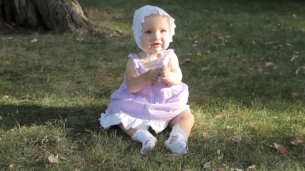 Una bambina con un cappellino seduta sull'erba illuminata dal sole al tramonto — Video Stock