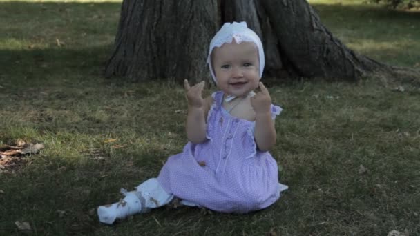 Una niña sonriendo, sentada en la hierba y aplaudiendo — Vídeos de Stock