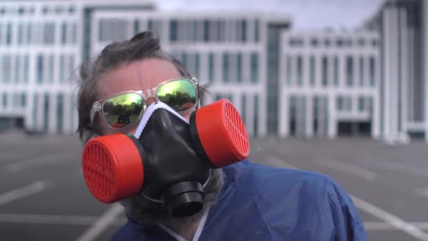 Skäggig man med solglasögon, respirator och skyddsdräkt ser ut att sola, tar av sig glasögonen och tittar på kameran Närbild — Stockvideo