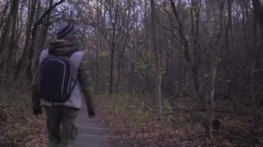 Sırt çantalı, askeri kargo pantolonlu ve asker botlarıyla orta yaşlı bir adam, Covid salgını sırasında parkta tek başına yürüyor.