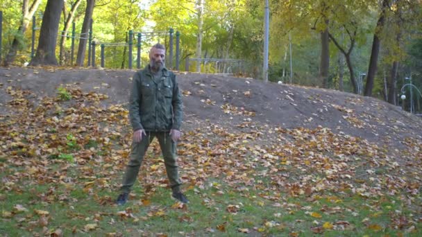 Vousatý muž středního věku v khaki oblečení cítí bolest zad během cvičení v podzimním městském parku — Stock video