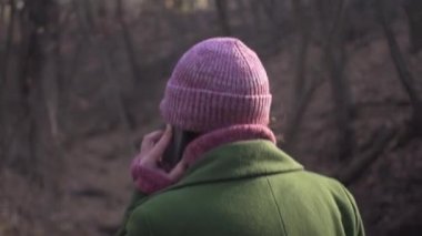 Kırmızı şapkalı orta yaşlı bir kadın akıllı telefonuyla konuşuyor. Salgın koronavirüs kilitlenmesi sırasında orman parkında tek başına yürüyor.