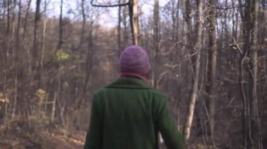 Kırmızı şapkalı ve yeşil ceketli orta yaşlı bir kadın Covid pandemik koronavirüs kilitlenmesi sırasında orman parkında asfalt yolda yürüyor.