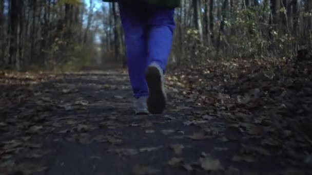 Visão baixa das pernas femininas em tênis brancos e jeans azuis correndo ao longo do caminho do parque florestal na solidão durante o bloqueio do coronavírus — Vídeo de Stock