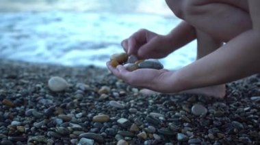 Sahilde gün batımında çakıl toplayan orta yaşlı kadın elleri.