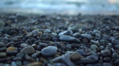 Yakın plan mavi, orta yaşlı kadın bacakları çakıl taşlı sahil kıyısı boyunca soldan sağa yürüyor.