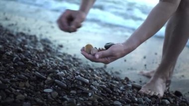 Gün batımında kumsalda çakıl taşları toplayan orta yaşlı kadın elleri.