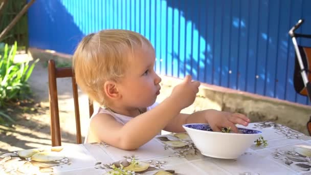 Malá blondýnka dítě jíst hrozny u stolu ve dvoře domu v létě — Stock video