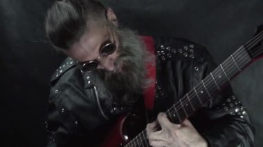 Tıraşlı şakakları olan yuvarlak gözlükler takan rock müzisyeninin yakın çekimi konserde kırmızı elektro gitar çalıyor.