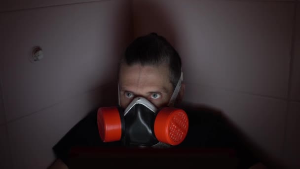 Uomo barbuto di mezza età in respiratore rosso guarda intensamente nascondersi da tutti in bagno scuro — Video Stock