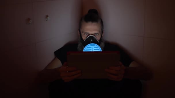 Uomo di mezza età in blu respiratore divertente guardando cattive notizie di infezione da malattia pericolosa su tablet in bagno scuro — Video Stock