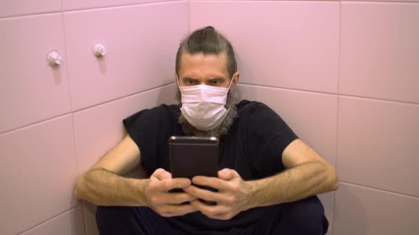 Homem barbudo de meia-idade em máscara médica chocou más notícias de infecção perigosa doença assistindo no smartphone se escondendo de todos no banheiro — Vídeo de Stock