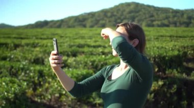 Güzel bir kadın, taze yeşil çay tarlasında akıllı telefondan selfie çekiyor.