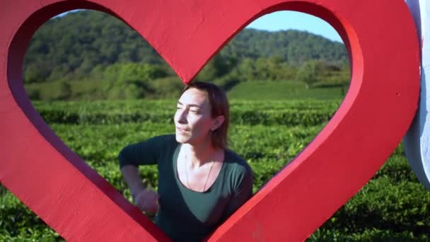 Beatiful atractiva joven en gran corazón rojo con fondo de campo de plantación de té verde fresco — Vídeo de stock