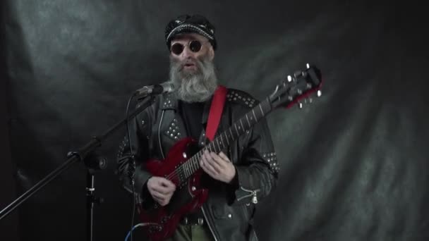 Rockstar, одягнений у шкіряну куртку, грає на червоній електрогітарі і співає на сцені з чорним фоном. — стокове відео