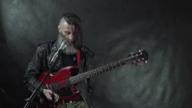 Tıraşlı şakakları, sakalı ve deri ceketi olan rock yıldızı çalmayı kes ve kırmızı elektro gitarı çıkar.