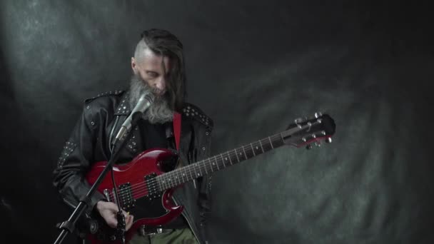 Rockstar con varillas afeitadas, la barba y la chaqueta de cuero dejan de jugar y se quita la guitarra eléctrica roja — Vídeo de stock