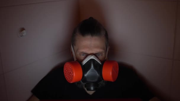 Бородатый мужчина средних лет в красном респираторе прячется в темной ванной, читая о ковиде в социальных сетях — стоковое видео