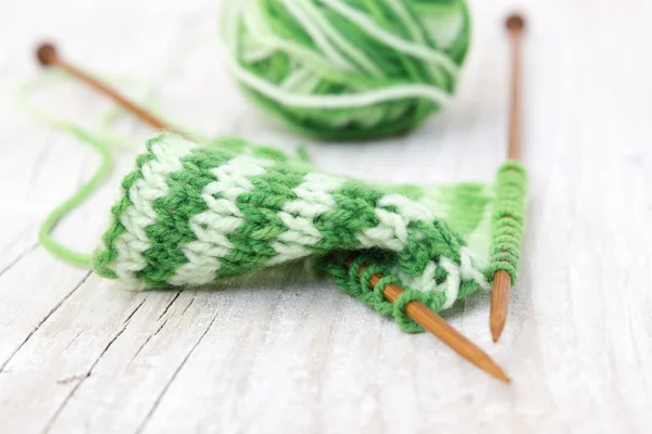 Knitting pattern of green yarn on wooden needles and skein — Stock Photo, Image