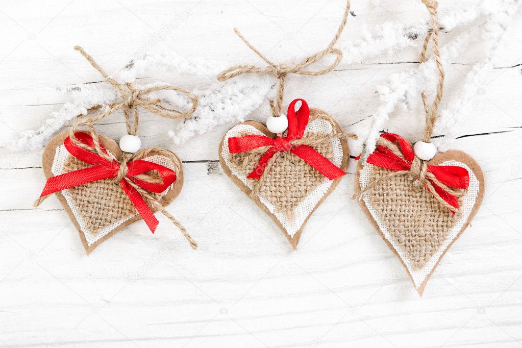 Decorative hearts on snow-covered branch on wooden background