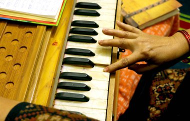 Bir insanın eli harmonyum çalarken yakın plan görüntüsü, tuşları ve ahşap tasarımı vurguluyor.