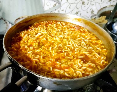 Çelik bir tavada kaynar suda pişen hazır eriştelerin yakın çekim görüntüsü.