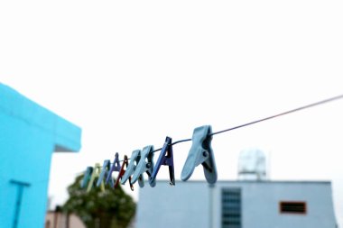 Bir grup renkli mandal, açık hava konut ortamında çamaşır ipine takılmış..