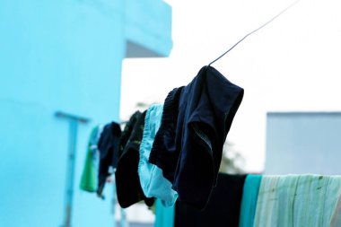 Çamaşır giysileri, parlak mavi bir duvara karşı güneş ışığı altında kurutmak için ipe asılmış.