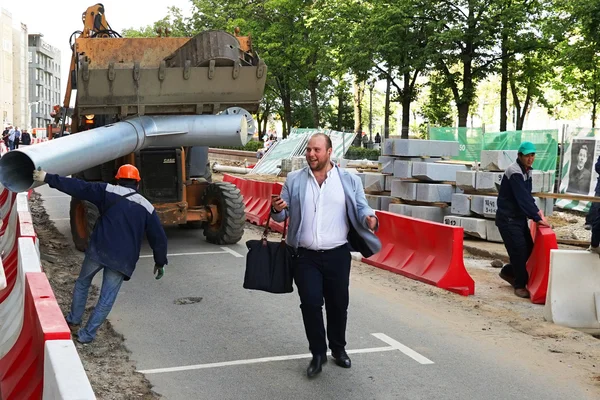 MOSCÚ, RUSIA - 15 DE MAYO DE 2016: Riendo hombre con un teléfono inteligente y una bolsa negra en un sitio de construcción. Reconstrucción de la carretera dentro del programa de embellecimiento de la ciudad My Street in Moscow . —  Fotos de Stock