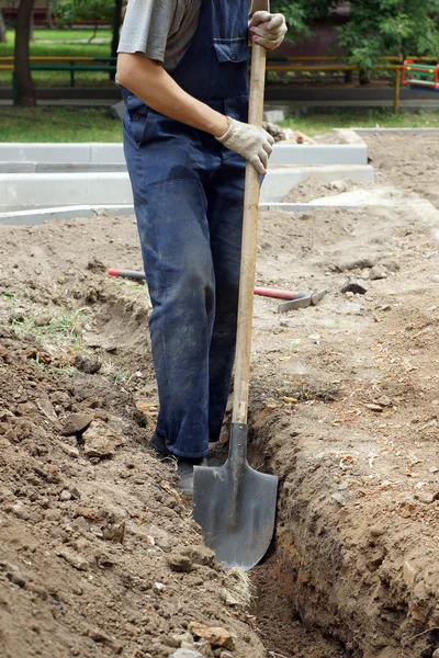 Arbeiter in Overalls gräbt mit Schaufel ein Loch in den Boden — Stockfoto