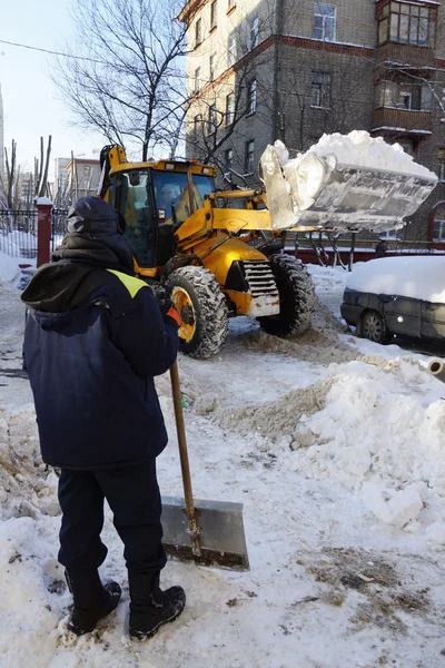 Een man met een schop lijkt een trekker wordt gewist sneeuw — Stockfoto