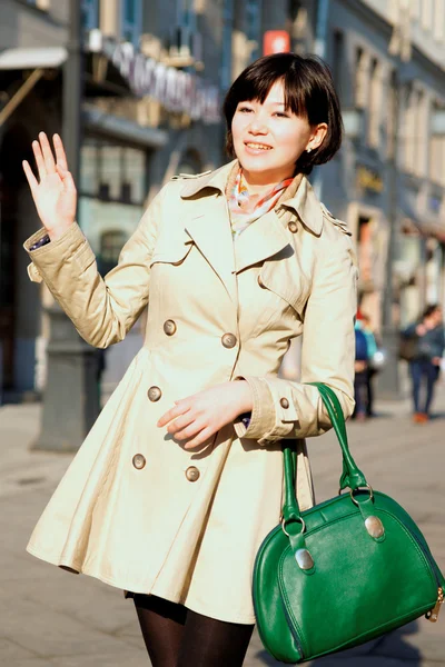 The girl with the green bag is smiling and waving. — Stock Photo, Image