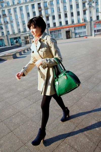 Chica en un impermeable ligero y bolsa verde, caminando por la calle . — Foto de Stock