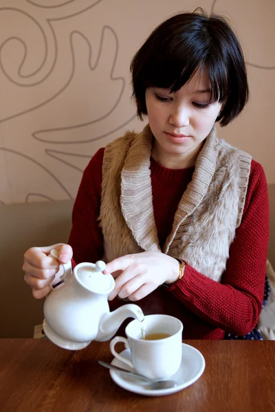 Frau gießt Tee aus Wasserkocher in Tasse. — Stockfoto