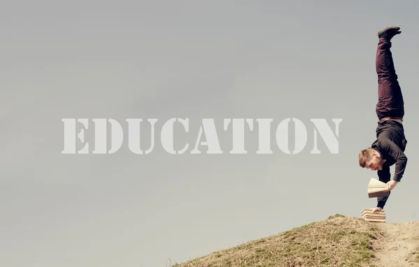 Idea de educación. Chico de pie sobre su cabeza y leyendo — Foto de Stock