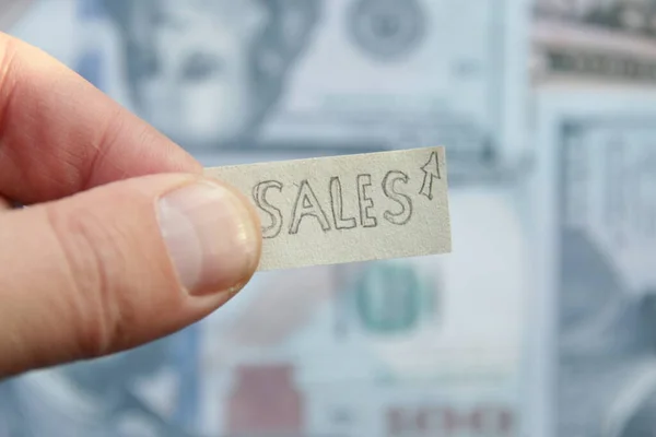 Concepto de crecimiento de ventas Una mano sostiene una etiqueta en el fondo de los billetes. — Foto de Stock
