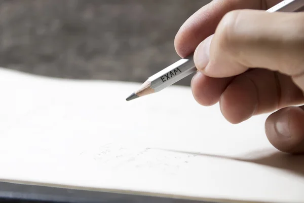 Student writing a test, an inscription on pencil "exam" — Stock Photo, Image