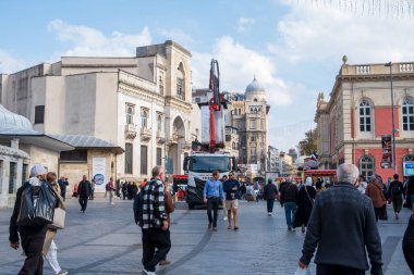 10.17.2025, İstanbul, Türkiye. Güneşli bir günde tarihi Osmanlı mimarisinin önünden geçen vinç kamyonları ve yayalarla dolu Eminn Meydanı İstanbul, geleneksel binalarla kentsel sokak manzarası