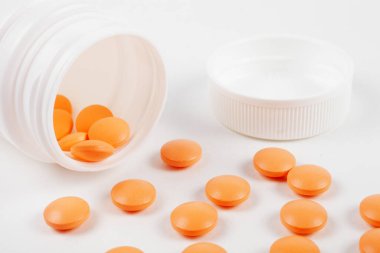 Tabletlerdeki turuncu vitaminler beyaz bir masanın üzerinde, yakın plan. 