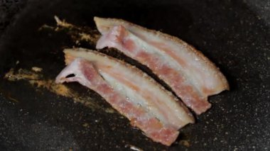 Şef bir tavada iki parça pastırma kızartır, yakın plan. 