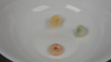 yuvarlak renkli tanecikler beyaz bir tabağa düşer, yakın plan. 