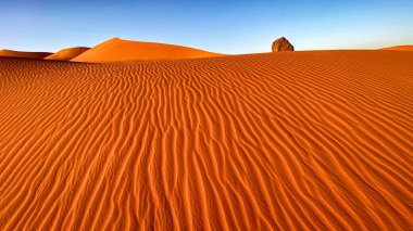 Cezayir, Sahra Çölü 'ndeki Kızıl Tadrart manzarası. Kum tepelerinden bir kaya çıkıyor. Rüzgâr kumdaki dalgaları şekillendirdi.