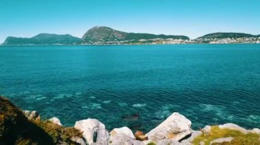 Very slow and low flight over the rocky beach. Clear, azure water and sunny weather. The sea and mountains in the background. Norway 2020.