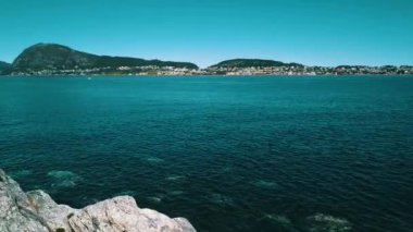 Kayalık sahil üzerinde uçuş. Temiz, masmavi bir su ve güneşli bir hava. Arka planda deniz ve dağlar var. Norveç 2020.
