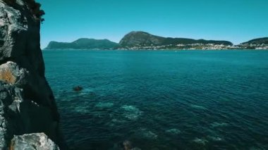 Kayalık sahil üzerinde uçuş. Temiz, masmavi bir su ve güneşli bir hava. Arka planda deniz ve dağlar var. Norveç 2020.
