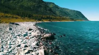 Kayalık sahil üzerinde uçuş. Temiz, masmavi bir su ve güneşli bir hava. Arka planda deniz ve dağlar var. Norveç 2020.