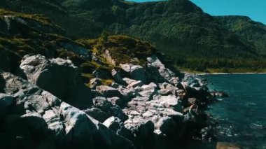 Kayalık sahil üzerinde rotalı uçuş ve... Temiz, masmavi su, yeşil bitki örtüsü ve güneşli hava. Arka planda deniz ve dağlar var. Norveç 2020. Arka planda deniz ve dağlar var. Güneşli bir yaz gününde İHA ile çekilmiş..