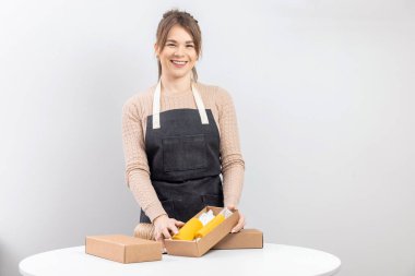 Önlüklü usta kadın, paketlenmiş, bal kokulu bal kokulu, arıdan yapılmış sarı mumlar tutuyor.