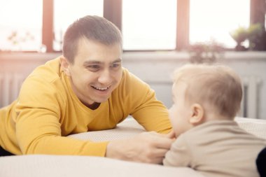 Genç baba yeni doğmuş bebekle yatakta oynuyor.